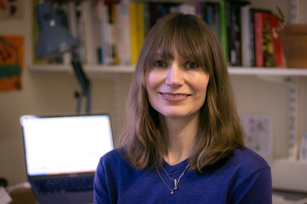 A White woman in a blue top with brown hair and a fringe smiles at the camera. She is Dr Morgan Currie.