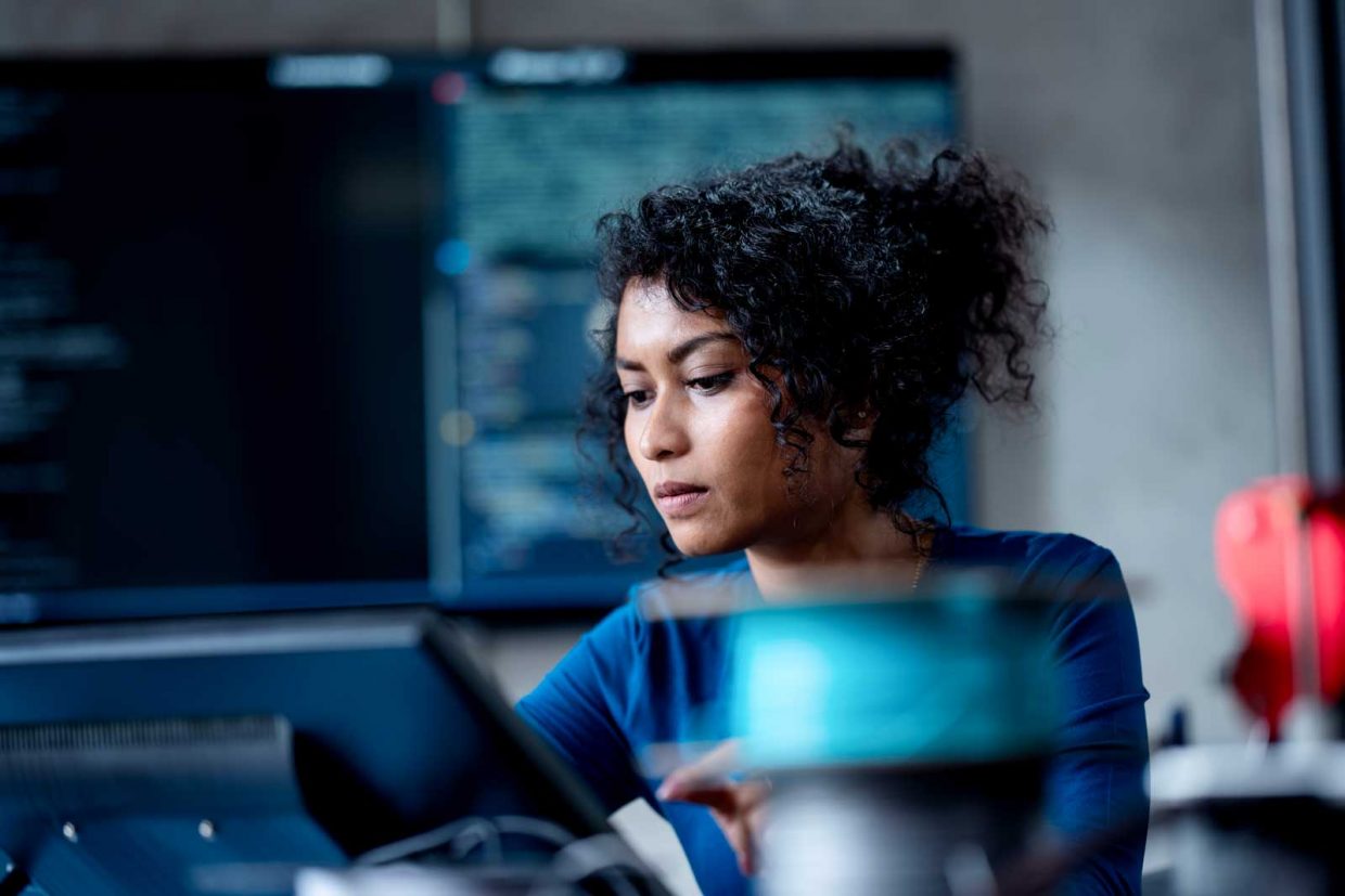 A photograph of a person working at the computer desk with a big screen behind.