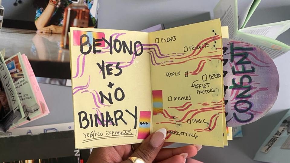 An image of a yellow paper zine in someone's hand. The zine shows the words "beyond yes and no binary".